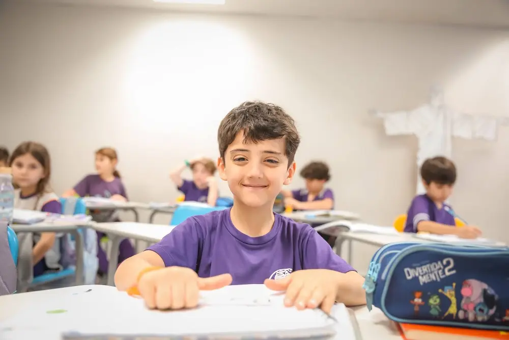 Aluno da Evolution Teens sorrindo na carteira durante a aula