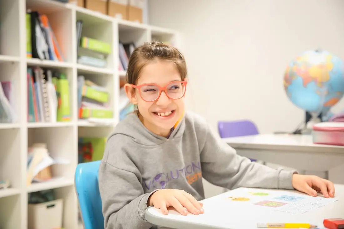Aluno da Evolution Teens sorrindo ao lado de um globo, na sala de leitura