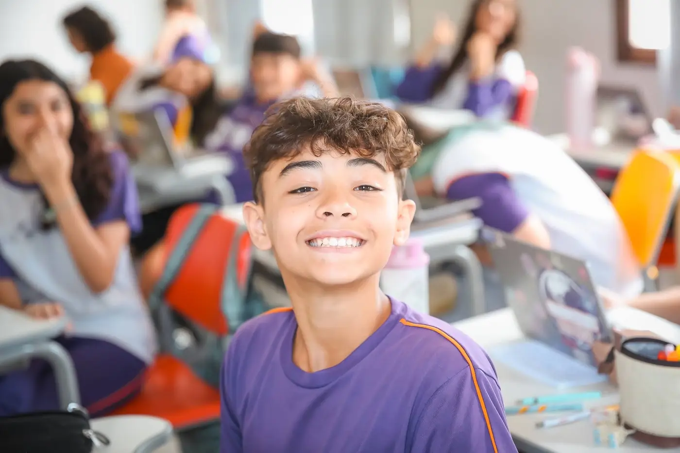 Aluno da Evolution Teens sorrindo em sala de aula com os colegas